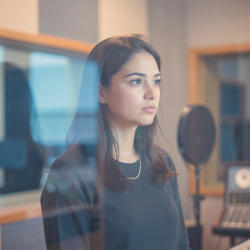 Une jeune chanteuse dans un studio d’enregistrement baigné de lumières bleues et ambrées, avec une atmosphère floue et introspective.